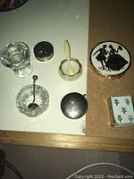 Top view of vintage vanity items including glass jars, metal tins, compact powders, decorative box, and small spoon