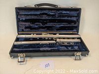 Closed case with flute parts arranged inside the fitted blue velvet interior, including body, foot joint, and head joint. Empty slot for piccolo visible.