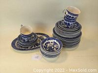 Stack of Blue Willow bowls, plates, cups, and saucers arranged with a few plates and an oval platter visible.