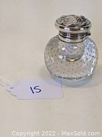 Front angled view of bubble glass inkwell with detailed sterling silver lid showing floral design and round clear glass body with embedded bubbles.