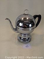 Front angle view of chrome Art Deco electric coffee percolator, showing reflective spherical body, curved spout, and black handle.