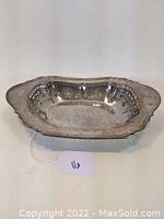 Angled view of the front side of the oblong silver reticulated bowl showing the pierced floral edges and the scalloped rim.