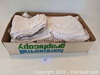 Box filled with folded vintage white linens including doilies and cloths