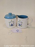 Front view of creamer and sugar container with lid, showing the Swiss Alpine floral pattern and blue interiors.