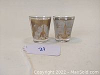 Pair of clear shot glasses with gold illustrations and lettering depicting the Empire State Building and surrounding New York City.