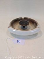 Side view of tri-cornered ashtray showing beige to brown gradient glaze and central metal knob with monogram.
