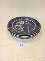 Stack of four Blue Willow dinner plates showing rim and side profile