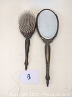 Hairbrush and hand mirror side by side on light background showing fronts with bristles and mirror surface.