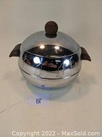 Front view showing engraved penguin designs on round polished metal ice bucket with walnut handles and lid knob.