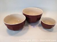 Set of three burgundy red ceramic mixing bowls of different sizes stacked together showing cream interiors.