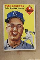 Front side of the 1954 Tommy Lasorda rookie card showing portrait, Dodgers insignia, name, and position with visible creases and edge wear.