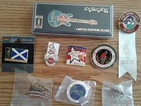 Photo showing entire set of nine trading pins from 1996 Atlanta Olympics, including limited edition Coca Cola guitar pin in plastic box and some pins in original plastic bags, plus a white ribbon labeled '1996 Olympic Games Pin Society Atlanta 1996'.