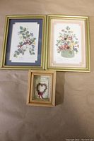 Three small framed flower prints displayed on a surface, two larger gold framed prints with double matting on top and one smaller wood framed print without matting below.