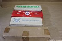 Photo showing four boxes of 1988 baseball sets stacked, including Fleer box on top, Score collector set, Topps puzzle and cards box, and an unidentified taped box below.