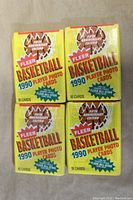 Four unopened 1990 Fleer Basketball wax packs arranged on a surface, showing front packaging with colorful graphics and text detailing contents.