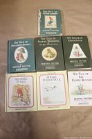Front view of all 7 hardcover Beatrix Potter books arranged in two rows showing cover art and titles. Peter Rabbit cover is visibly worn and damaged at edges.