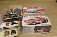 Overview photo showing two AMT plastic model kits in box (1968 Cadillac Convertible and 1957 Chevrolet Corvette Gasser) plus two partially assembled metal body car models with plastic parts scattered in tray.