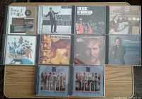 Overview photo showing 10 classic pop-rock CDs arranged in two rows on a flat wooden surface including The Mamas and The Papas, The Band, Mountain, Gordon Lightfoot and others.