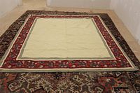 Photo showing entire large quilt laid out flat on a patterned rug, cream central area with red floral border visible