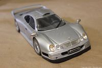 Angled front-side view of the silver Mercedes Benz CLK-GTR model car showing body detail and front grille with AMG logo.
