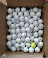 Top view of a box filled with over 160 used Pinnacle golf balls, mostly white with one yellow ball.