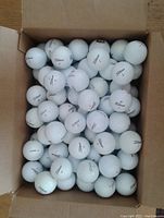 Box filled with approximately 100 used white Titleist golf balls with varying numbers and minor wear marks.