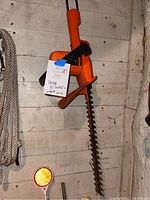Orange Black and Decker hedge trimmer with serrated cutting blade hung on wall.