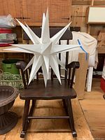 Child-sized wooden rocking chair with white light-up holiday star decoration on seat, wood panel background.