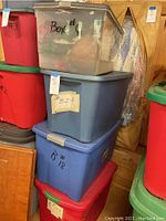 Full view of stacked red, blue, and clear plastic storage bins containing Christmas decorations, labeled with numbers and tags.