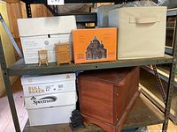 Shelf with various items including wooden dollhouse chair, wooden cabinet, dollhouse wiring kit box, and a wood chest below.