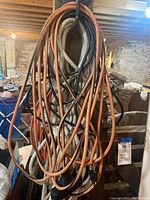 Two orange extension cords and one white braided rope hanging on a support beam in a basement or workshop area.