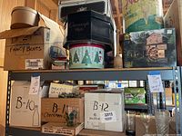 Shelf showing various boxes including hat boxes, fancy boxes, Christmas themed boxes, and puzzle boxes with some glassware visible on lower shelf.