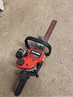 Red Homelite shrub trimmer with visible blade, handle, and control components on concrete floor.