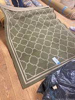 Rug partially rolled out, showing green color with beige trellis pattern and border