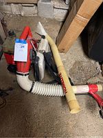 Side view of the red and white gas powered Homelite leaf blower resting on the ground with attached beige flexible hose and rigid tube extension.