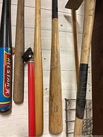 Photo showing three wooden baseball bats and two gardening tools against a wooden wall.