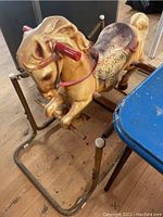 Full side view of the vintage rocking horse showing the golden tan molded horse figure mounted on rusty metal spring frame with red handles.