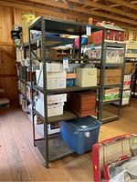 Photo of a 5 tier metal shelving unit filled with various boxes and storage containers, located in a large wooden room under construction or a warehouse space.