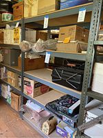 Photo shows 5 tier metal shelving unit loaded with various boxes and items for scale reference. Shelves made of particle board or wood panel with dark metal frame.