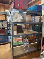 Photo of a 5 tier metal shelving unit with metal frame and wide shelves. Contains various storage boxes and containers, but these contents are not included in the lot.