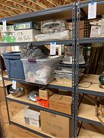 Photo shows a large metal shelving unit with five shelves containing various storage bins, boxes, and kitchen-related items, illustrating the shelving unit's size and structure.