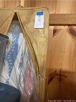 Photo of beige fabric storage cover showing zippered enclosure and partial glimpse of several plastic-covered tablecloths inside.