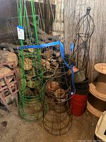 Green and black metal wire tomato cages with blue straps and assorted plant pots stacked and placed on wood logs background