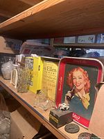 Shelf displaying vintage Coca-Cola trays, glassware, and small collectibles including toy car and decorative coins.
