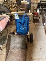 Front view showing metal wheelbarrow in front and Zoom Buggy beach cart behind it, highlighting wheelbarrow bucket and buggy blue fabric and handle.