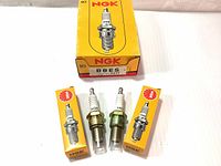 Ten new NGK spark plugs with yellow NGK boxes, two spark plugs outside of individual boxes.