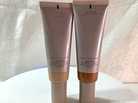 Two tubes of Laura Mercier Tinted Moisturizer Illuminating Natural Skin Perfector with labels showing - Pearl Radiance and Golden Radiance shades, each 50ml.