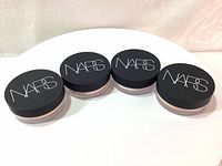 Four jars of NARS Soft Velvet Loose Powder placed in a row showing black lids with white NARS logo.