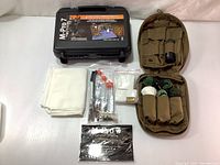 Black M-Pro 7 lockable plastic case, tan MOLLE pouch containing brushes and boresnake, white lint free cloth, cleaning patches, and cleaning rods with orange caps.