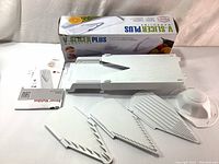 Photograph of Borner V-Slicer Plus mandoline set, showing the main white plastic body, three interchangeable blades arranged in front, safety holder with protective guard, instruction manual, and original box.